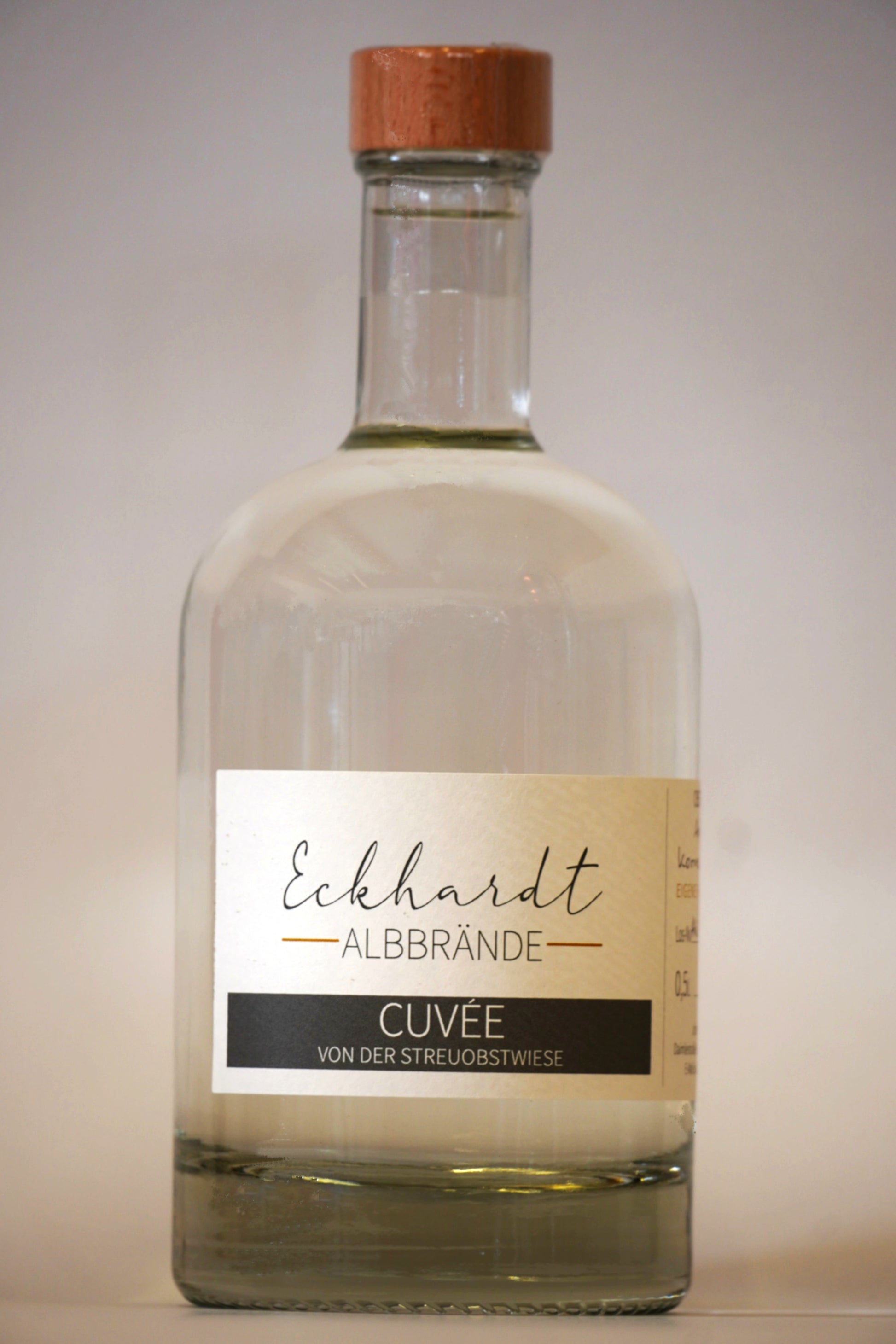 Glasflasche mit Holzdeckel vor einem weißen Hintergrund. Auf dem eleganten Etikett steht der Schriftzug "Eckhardt Albbrände" und die Bezeichnung "Cuvée von der Streuobstwiese".