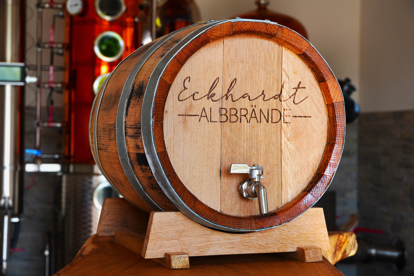 Ein hölzernes Fass steht vor einer Brennereianlage. Es trägt die Aufschrift "Eckhardt Albbrände".