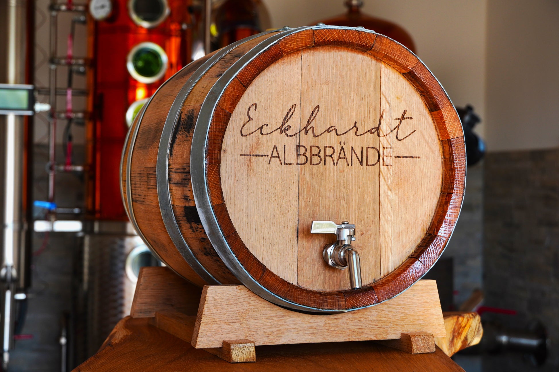 Ein hölzernes Fass steht vor einer Brennereianlage. Es trägt die Aufschrift "Eckhardt Albbrände".
